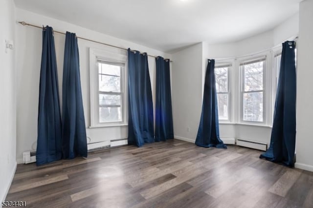 empty room featuring dark wood-type flooring, a baseboard radiator, and plenty of natural light