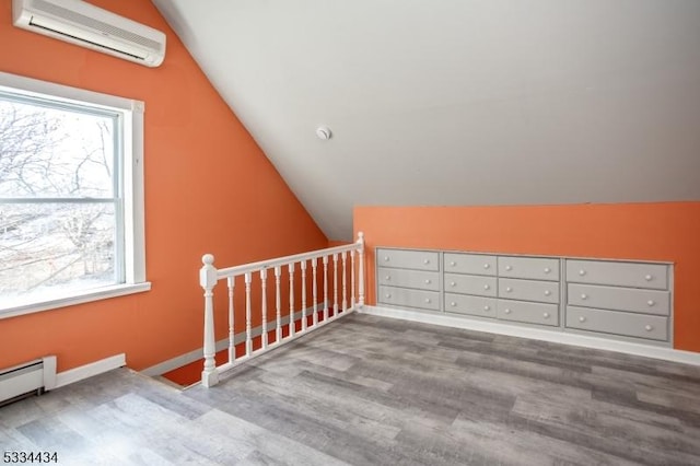 additional living space featuring light hardwood / wood-style flooring, vaulted ceiling, a wall unit AC, and a baseboard heating unit