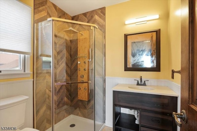 bathroom featuring toilet, a stall shower, vanity, and wainscoting