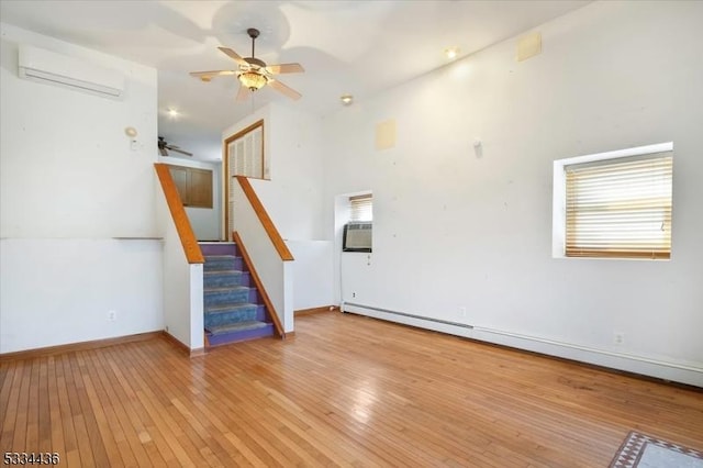 unfurnished living room with a ceiling fan, a baseboard radiator, stairway, a wall mounted air conditioner, and light wood-style floors