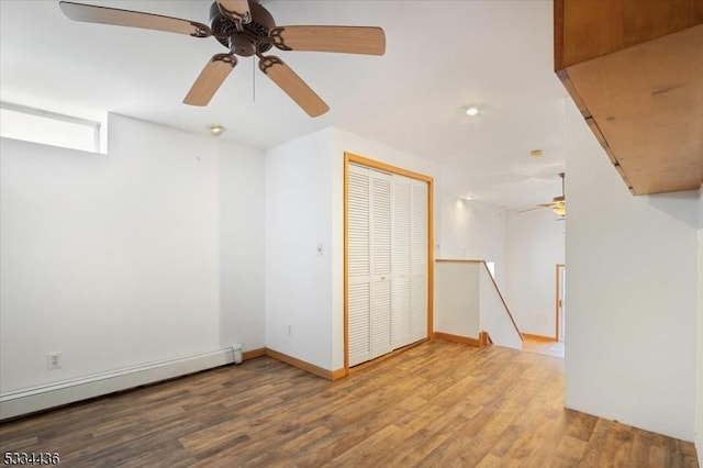 unfurnished room with baseboard heating, wood finished floors, and baseboards