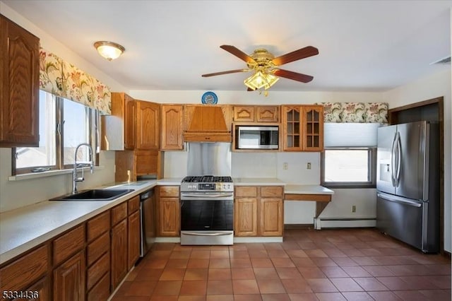 kitchen featuring stainless steel appliances, a sink, light countertops, brown cabinetry, and glass insert cabinets