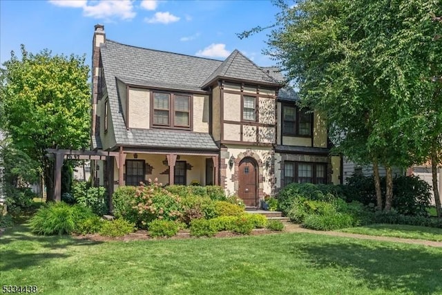 english style home featuring stucco siding, a pergola, a high end roof, a front yard, and a chimney