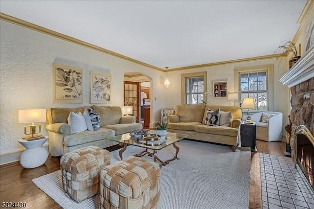 living room featuring arched walkways, a stone fireplace, wood finished floors, and ornamental molding