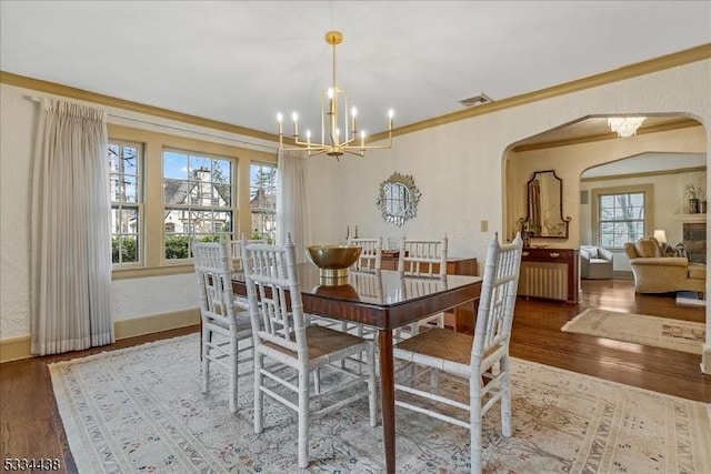 dining area with an inviting chandelier, crown molding, wood finished floors, and arched walkways