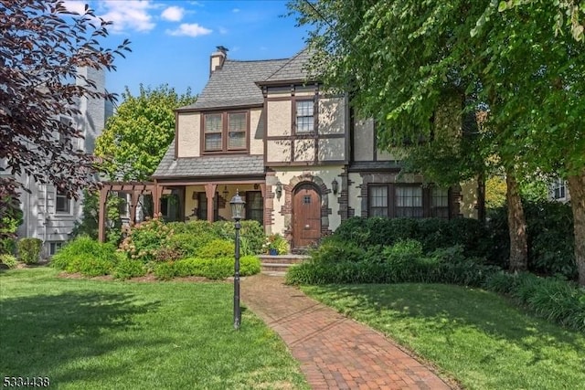 english style home with stucco siding, a front lawn, a pergola, a high end roof, and a chimney