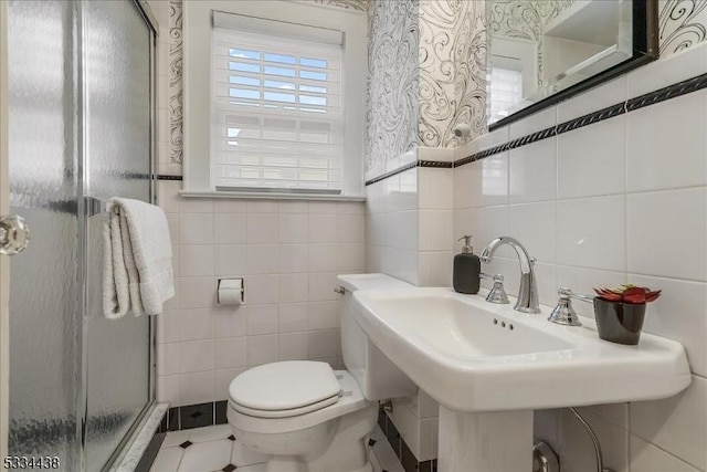 bathroom featuring a shower stall, toilet, tile patterned floors, tile walls, and a sink