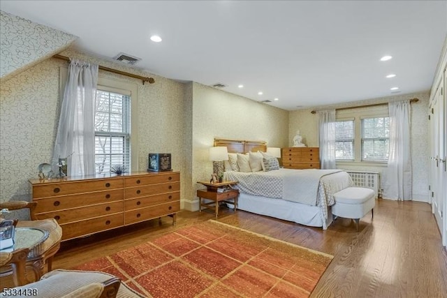 bedroom with wallpapered walls, multiple windows, wood finished floors, and visible vents