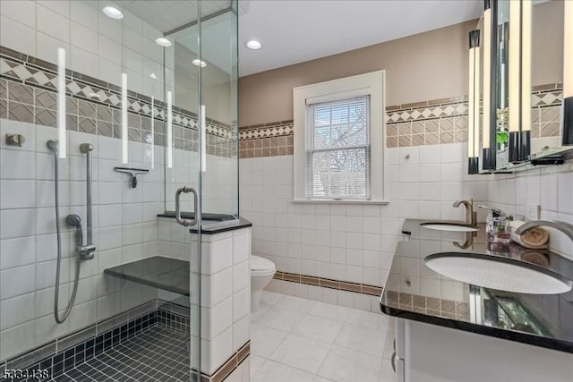 full bath featuring tile patterned floors, a sink, tile walls, a shower stall, and double vanity