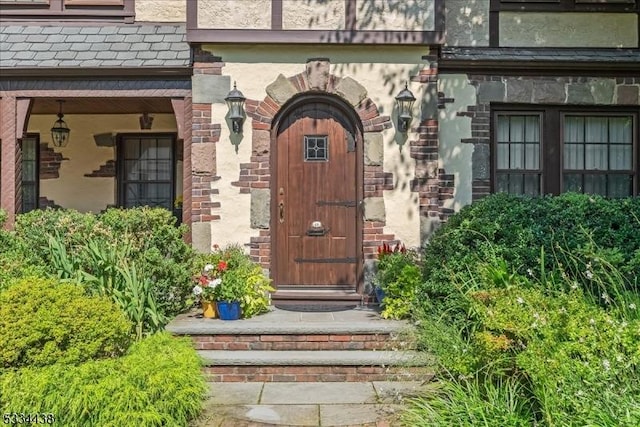 property entrance featuring brick siding, a high end roof, and stucco siding