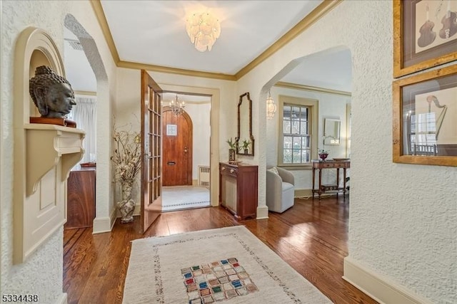 foyer entrance featuring arched walkways, wood finished floors, crown molding, and a textured wall