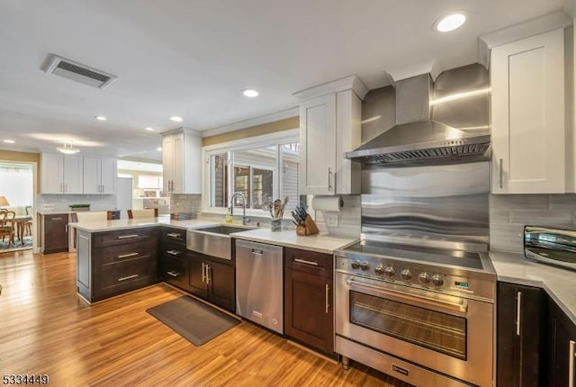 kitchen featuring white cabinetry, wall chimney range hood, decorative backsplash, and appliances with stainless steel finishes