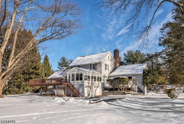 snow covered rear of property with a garage, a sunroom, and a deck