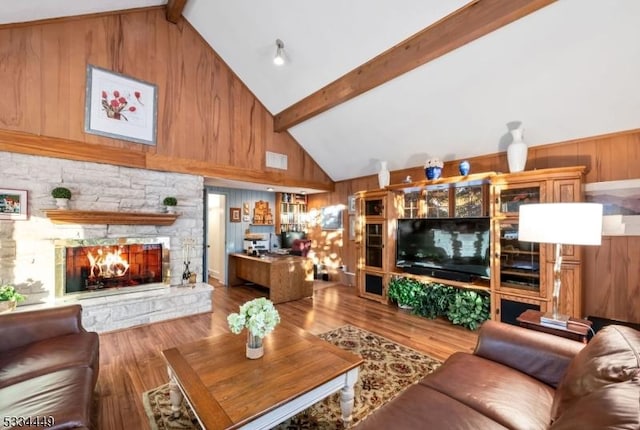 living room with wood-type flooring, a stone fireplace, high vaulted ceiling, and beam ceiling