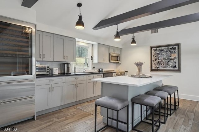 kitchen featuring appliances with stainless steel finishes, pendant lighting, sink, gray cabinetry, and vaulted ceiling with beams