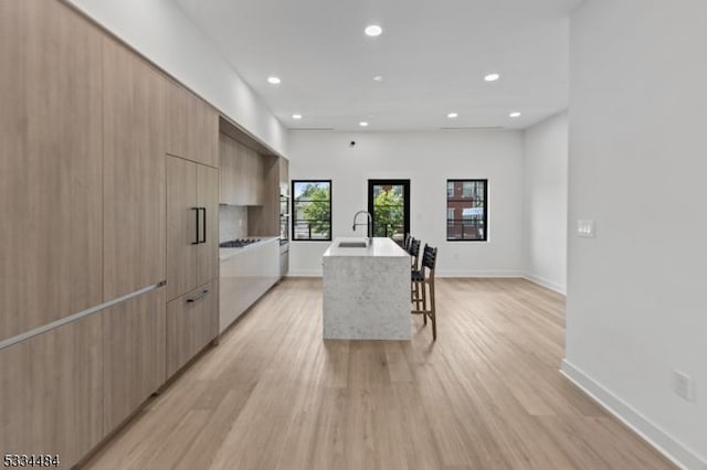 kitchen featuring light brown cabinetry, sink, light hardwood / wood-style flooring, a kitchen breakfast bar, and an island with sink