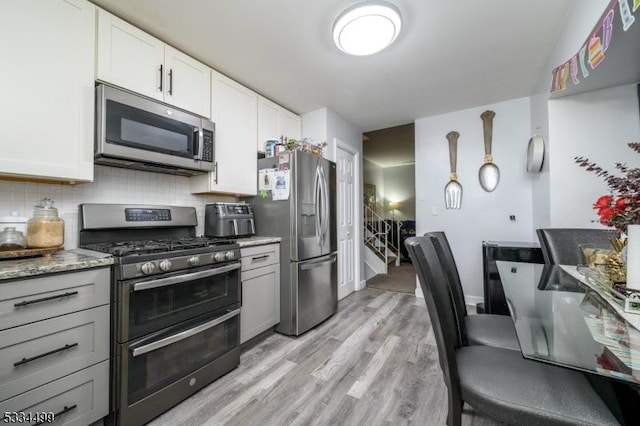 kitchen featuring white cabinetry, light wood-type flooring, stainless steel appliances, light stone countertops, and decorative backsplash