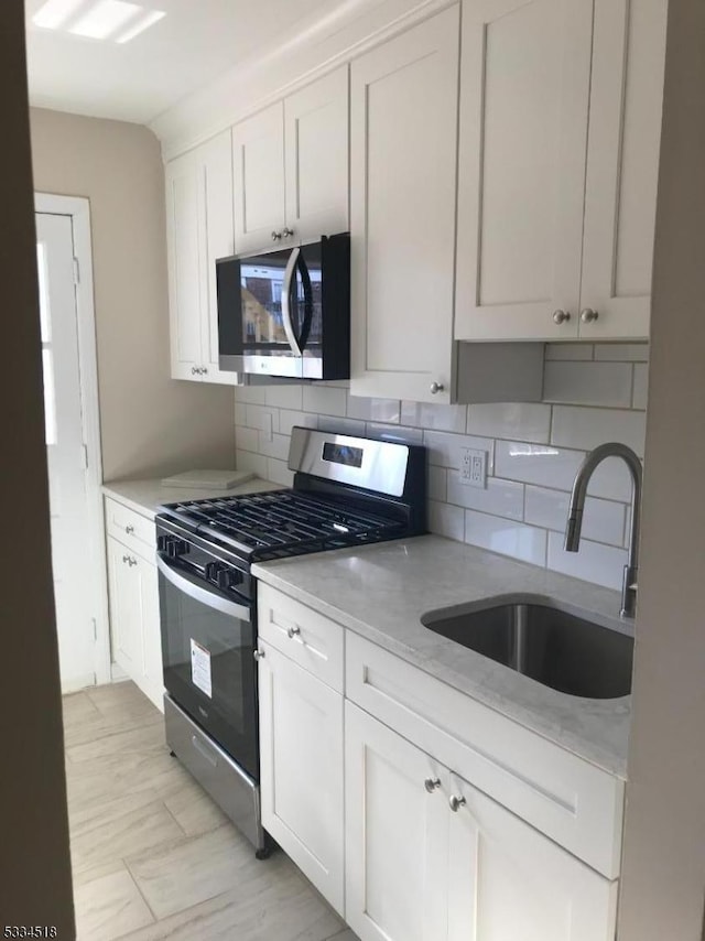 kitchen featuring sink, white cabinetry, light stone counters, stainless steel appliances, and backsplash