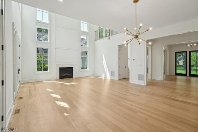 unfurnished living room featuring light wood-type flooring, an inviting chandelier, and a towering ceiling