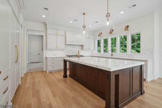 kitchen featuring hanging light fixtures, premium range hood, decorative backsplash, light hardwood / wood-style floors, and white cabinetry