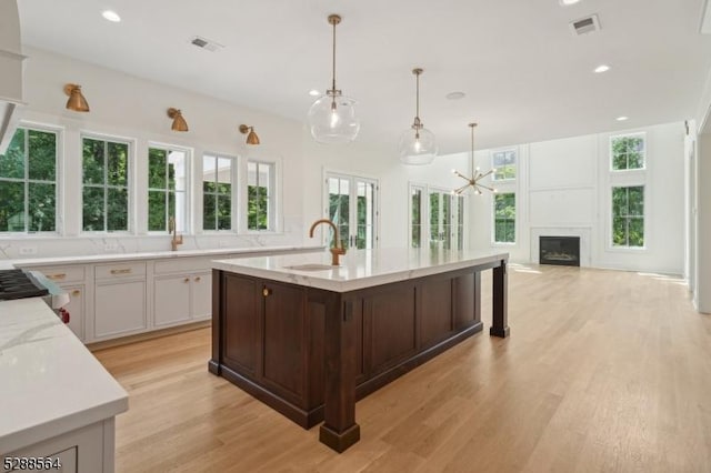 kitchen featuring light hardwood / wood-style flooring, decorative light fixtures, light stone countertops, sink, and white cabinets