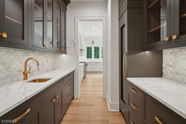 kitchen with light hardwood / wood-style flooring, sink, light stone counters, and decorative backsplash