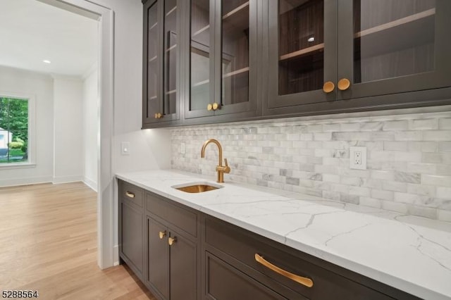 bar with light hardwood / wood-style flooring, sink, light stone counters, and tasteful backsplash