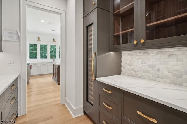 bar featuring light wood-type flooring, tasteful backsplash, and light stone countertops