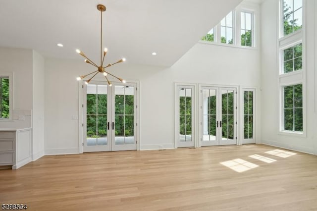 unfurnished living room with light hardwood / wood-style floors, a chandelier, a high ceiling, and french doors