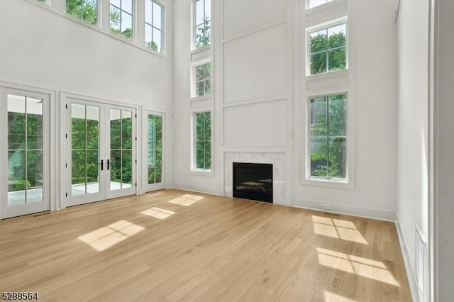 unfurnished living room featuring light hardwood / wood-style flooring, a high ceiling, french doors, and a high end fireplace