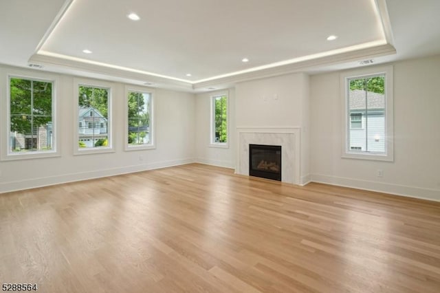 unfurnished living room featuring a raised ceiling, light wood-type flooring, and a high end fireplace