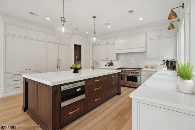 kitchen with an island with sink, double oven range, dark brown cabinets, white cabinets, and wall chimney exhaust hood