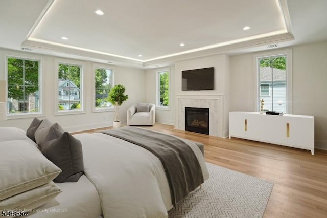 bedroom with a tray ceiling, light hardwood / wood-style floors, multiple windows, and a high end fireplace