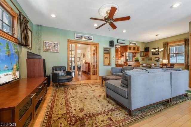 living room featuring ceiling fan with notable chandelier and light hardwood / wood-style flooring