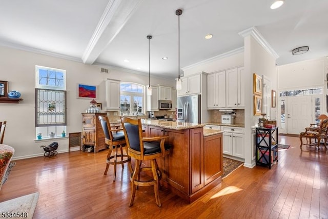 kitchen with crown molding, hanging light fixtures, appliances with stainless steel finishes, a kitchen island, and white cabinets