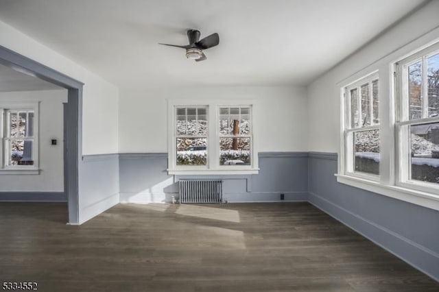 unfurnished dining area featuring dark hardwood / wood-style flooring, ceiling fan, radiator heating unit, and a healthy amount of sunlight