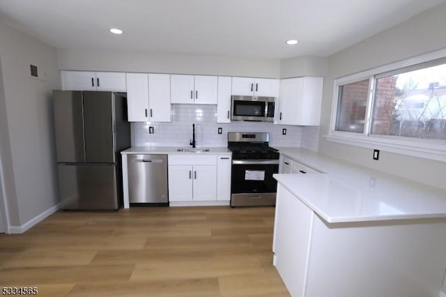 kitchen with sink, white cabinetry, light wood-type flooring, appliances with stainless steel finishes, and decorative backsplash