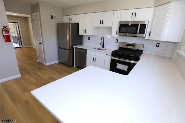 kitchen with stainless steel appliances, kitchen peninsula, sink, and white cabinets