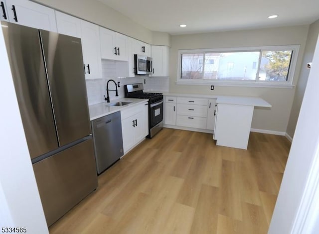 kitchen featuring appliances with stainless steel finishes, tasteful backsplash, white cabinetry, sink, and light hardwood / wood-style flooring