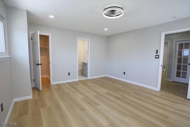 unfurnished bedroom featuring a walk in closet, ensuite bathroom, a closet, and light wood-type flooring