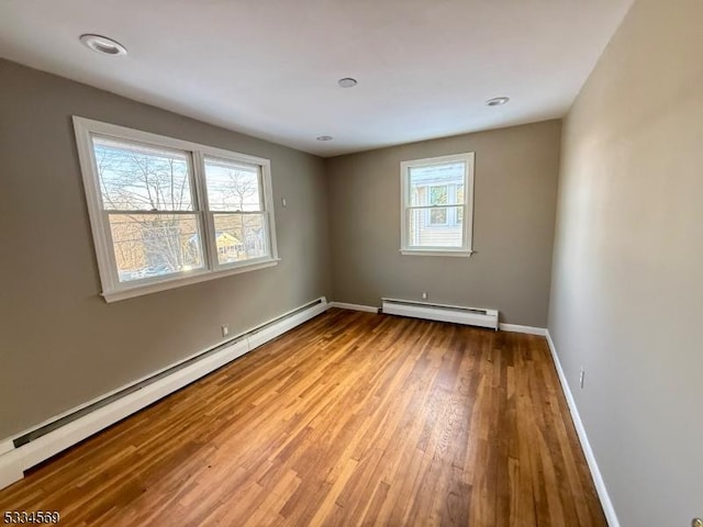 spare room featuring a baseboard heating unit and light hardwood / wood-style flooring