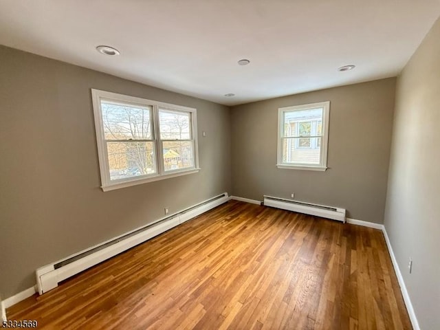 unfurnished room featuring baseboard heating and light hardwood / wood-style floors