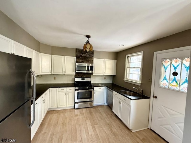 kitchen featuring appliances with stainless steel finishes, white cabinetry, sink, hanging light fixtures, and light wood-type flooring