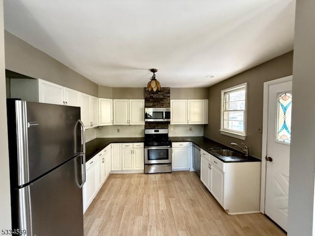 kitchen with sink, white cabinetry, decorative light fixtures, appliances with stainless steel finishes, and light hardwood / wood-style floors