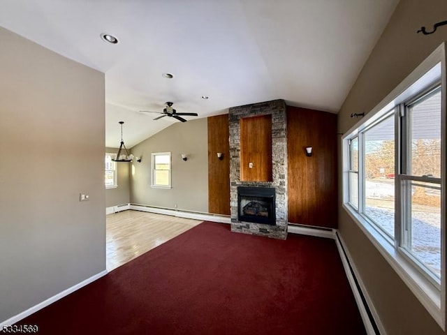 unfurnished living room featuring vaulted ceiling, a stone fireplace, a baseboard heating unit, and ceiling fan with notable chandelier