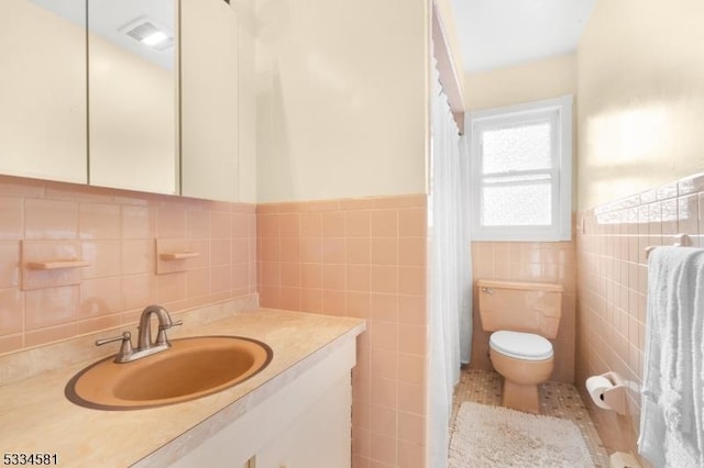 bathroom with vanity, toilet, and tile walls