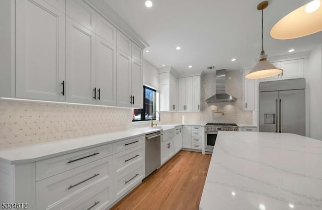 kitchen featuring pendant lighting, wall chimney range hood, white cabinetry, high quality appliances, and light stone countertops