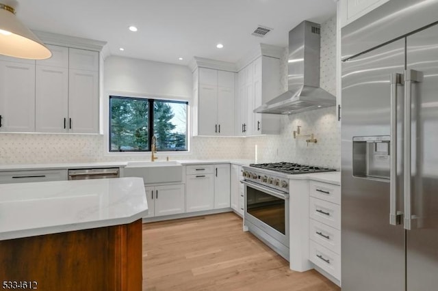 kitchen with sink, white cabinets, high end appliances, light hardwood / wood-style floors, and wall chimney range hood