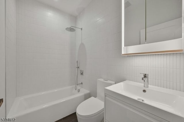 full bathroom with tiled shower / bath, vanity, toilet, and tile walls