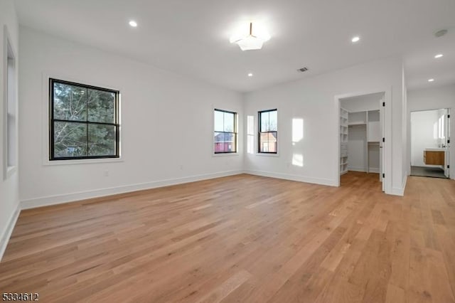 unfurnished bedroom featuring a walk in closet, a closet, and light hardwood / wood-style flooring